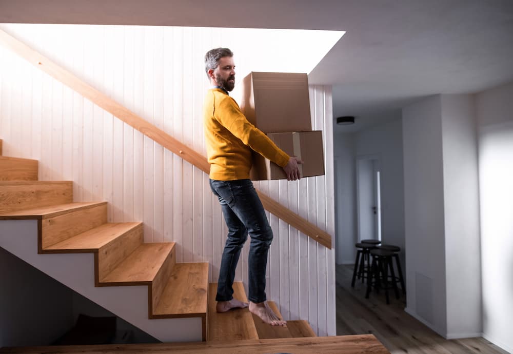 A man bringing down a stack of boxes downstairs.